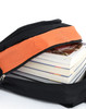 A black backpack with an orange accent unzipped to reveal stacked magazines inside.