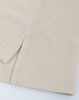 A close-up of a beige cotton/poly pique fabric, showcasing its texture and stitching details. It features a simple hemline.