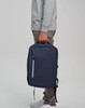 A navy blue PU backpack is being held by a person. The backpack features a zipper and has a logo.