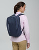 A navy blue backpack with a sleek design is worn by a person facing away, showcasing its minimalist style.