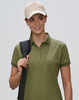 A woman wearing a khaki polo shirt and a beige cap, holding a black strap over her shoulder. The cap has a logo.