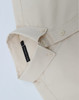 A beige men's long-sleeve shirt featuring a collar and buttons, with a branding label on the inside.