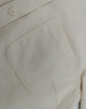 A close-up of a light beige cotton blend long-sleeve shirt, featuring a chest pocket and a button detail.