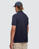 A man wearing a navy ultrafine cotton pique polo shirt, viewed from the back, paired with light-coloured trousers.