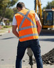 A safety vest in bright orange with reflective stripes, worn by a worker operating machinery on a construction site.