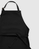 A black apron with adjustable straps and a waist tie, featuring a simple and sleek design.