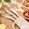 A calico pouch containing biodegradable cutlery: a fork, knife, and spoon in a light beige colour, set on a woven placemat.