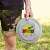 A person holds a translucent gray frisbee featuring colorful text and a logo. The background shows green grass.