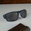 A pair of blue sunglasses with dark lenses rests on a light surface beside a brown case.