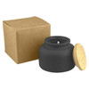 A black candle in a round jar with a bamboo lid, accompanied by a brown cardboard box.