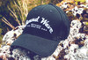 A black cap with a white embroidered logo, featuring the words "Sound Wave" and stars, resting on rocky terrain.