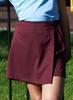 A maroon school skort with a side wrap design, displayed on a person against a green background.