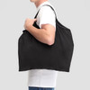 A black nylon shopper bag is being held by a person, featuring a simple and spacious design.