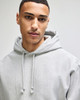 A grey hooded sweatshirt with a drawstring hood, featuring a logo. The model has short dark hair.