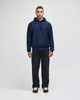 A navy blue pullover hooded sweatshirt with a front pocket and drawstring hood, paired with dark trousers.