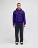 A purple pullover hooded sweatshirt with a front pocket and a logo, paired with dark pants.