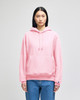 A pink pullover hooded sweatshirt with a front pocket and a branded logo. Model is wearing it with blue jeans.
