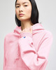 A pink hoodie with a drawstring hood and a logo on the sleeve. The model is looking directly at the camera.
