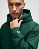 A green hooded sweatshirt with a logo on the sleeve, featuring a model showcasing its style and fit.