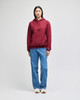 A model wearing a burgundy pullover hooded sweatshirt paired with light blue jeans, featuring a logo.