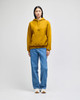 A model wearing a mustard yellow Champion Reverse Weave pullover hooded sweatshirt and blue jeans.