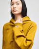A yellow pullover hooded sweatshirt with a logo, worn by a model standing against a light background.