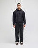 A black pullover hooded sweatshirt worn with matching dark trousers, featuring a logo on the sleeve.