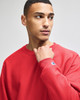 A red sweatshirt featuring a logo on the sleeve, modelled by a person looking to the side.