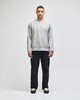 A grey crew sweatshirt worn by a model, paired with black trousers, featuring a subtle logo.