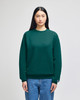 A green crewneck sweatshirt with a logo, displayed on a model wearing blue jeans.
