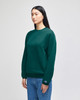 A green crewneck sweatshirt with a logo, worn by a model standing in front of a neutral background.