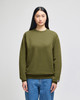 An adult crewneck sweatshirt in olive green, featuring a logo and styled with blue jeans.