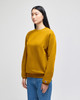 A mustard yellow crewneck sweatshirt is displayed on a model, featuring long sleeves and a logo on the cuff.