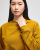 A model wears a mustard yellow Champion Powerblend® adult crewneck sweatshirt with a logo on the sleeve.