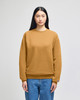 A model wears a mustard-coloured Champion Powerblend® crewneck sweatshirt, paired with blue jeans.