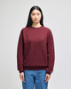 A maroon crewneck sweatshirt on a model, featuring a logo and styled with light blue denim jeans.