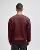 A crewneck sweatshirt in burgundy, featuring a back view and long sleeves, with a logo on the garment.