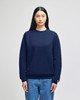 A navy adult crewneck sweatshirt is worn by a model, featuring a logo on the sleeve. The model pairs it with denim jeans.