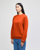 An orange adult crewneck sweatshirt displayed on a model, featuring a logo on the sleeve.