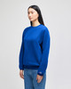 A blue crewneck sweatshirt on a model, featuring long sleeves and a logo on the cuff.