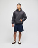 A model wears a grey crewneck sweatshirt with a hood, paired with navy shorts and casual shoes.