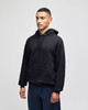 A black hooded sweatshirt with a front pocket and a hood, worn by a model. There is a logo on the garment.