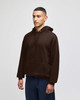 A brown pullover hooded sweatshirt with a front pocket and a logo, displayed on a model against a plain background.