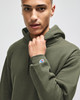 A green hooded sweatshirt with a fitted design and a small logo on the sleeve, worn by a model.
