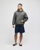 An adult pullover hooded sweatshirt in green, paired with navy shorts. The model stands confidently with one hand in the pocket.