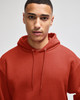 A hooded sweatshirt in a rusty red colour, featuring a relaxed fit and a drawstring hood. It has a logo on the front.