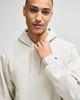 A light grey pullover hooded sweatshirt featuring a logo on the sleeve. Model wears it with a confident expression.