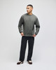 A man stands wearing a grey pullover hoodie, paired with black pants, showcasing a simple and casual style.