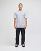 A model stands in a grey Champion adult short-sleeve T-shirt, paired with black pants. The shirt features a logo.