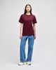 A model wearing a burgundy short-sleeve t-shirt, paired with blue jeans and white footwear. The shirt has a logo.